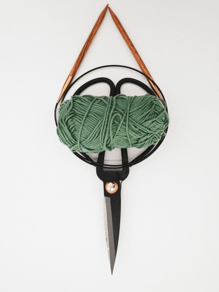 Pelote de laine verte suspendue à une paire de ciseaux décoratifs.